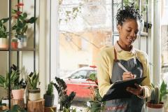 Une jeune fleuriste prend des notes manuelles debout au milieu de sa boutique