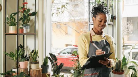 Une jeune fleuriste prend des notes manuelles debout au milieu de sa boutique