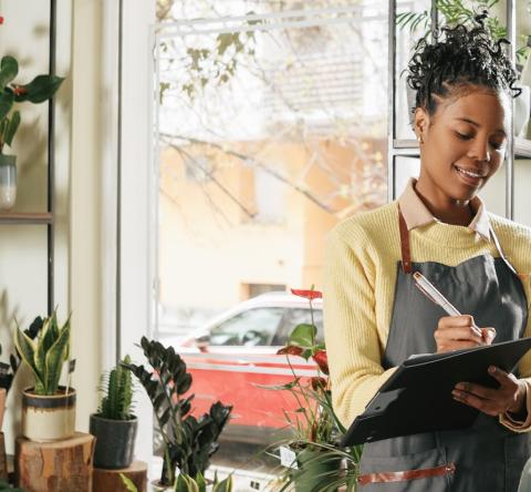 Une jeune fleuriste prend des notes manuelles debout au milieu de sa boutique